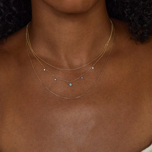 Close-up of layered gold necklace with blue opal drops and dainty chains on model