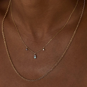 Close-up of layered gold necklaces featuring a blue opal teardrop pendant and O-chain