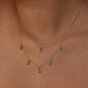 Detail of double-layer gold necklace with rectangular green gems and opal accents on neck
