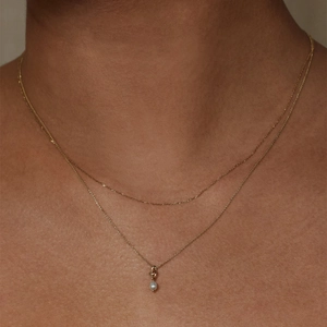 Close-up of double-layer gold necklace featuring a delicate chain and white pearl pendant