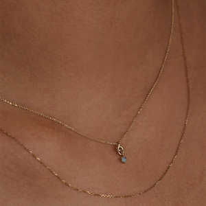 Detail of layered gold necklaces with blue opal pendant and twisted ring knot