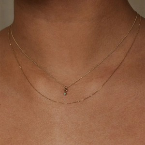 Close-up of gold layered necklaces featuring a delicate green gemstone pendant on model
