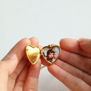 Close-up of a gold heart locket necklace being held open to reveal two tiny photos