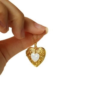 Gold heart locket necklace with floral engraving and opal stone on white background