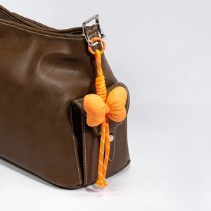 Handmade orange bow phone charm with metal clasp attached to a brown leather bag