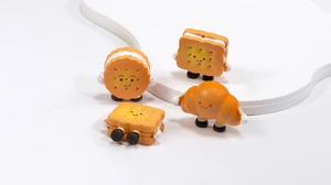 Detail of four cute acrylic cartoon biscuit and bread charms on a white display stand