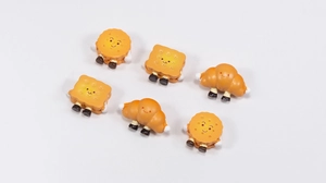 Macro shot of cute acrylic biscuit and croissant charms with cartoon faces and limbs