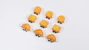 Flat lay of cute acrylic biscuit and croissant charms with cartoon faces on white background