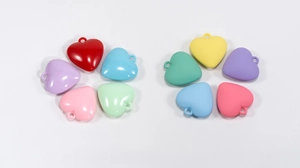 Dettaglio macro di ciondoli a cuore in acrilico con finiture lucide e opache color macaron