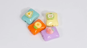 Close-up of four acrylic fruit candy charms for DIY jewelry in green, orange, yellow, and purple
