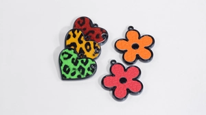 Dettaglio macro di ciondoli a cuore e fiori in acrilico con stampa leopardata e bordi neri
