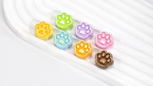 Close-up of seven colorful 3D cat paw charms on a white wavy tray for DIY jewelry