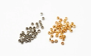 Makroaufnahme von 2,5mm Gold- und Silber-Quetschperlen für DIY-Schmuck auf weißem Grund