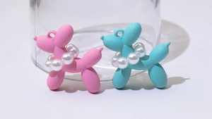 Nahaufnahme matter Ballon-Hund-Anhänger in Pink und Blau mit Perlenketten und Ringen