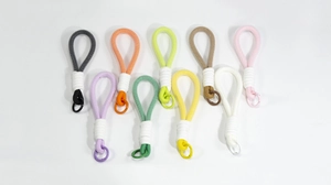Detail view of ten colorful hand-woven lanyards with metal ring hooks on a white surface