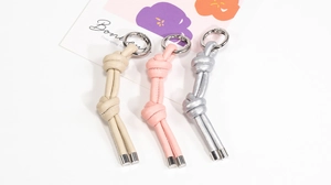 Dettaglio dei portachiavi in pelle intrecciata beige, rosa e argento con anelli
