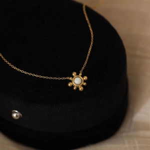 Close-up of a 18K gold sunflower necklace with a white opal stone on black velvet