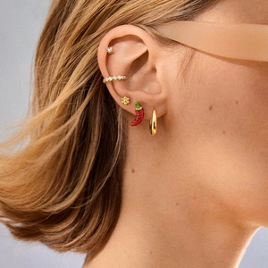 Close-up van sprankelende rode chili oorbellen en gouden zirkoon oorknopjes op model