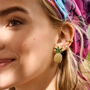 Macro detail van sprankelende ananas oorbellen en gouden ear cuff bij een model