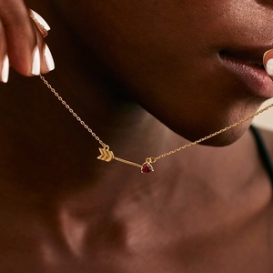 Close-up of golden arrow necklace with red heart stone on female model neck