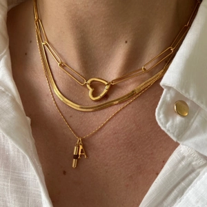 Close-up of layered gold necklace set with heart carabiner and letter A pendant