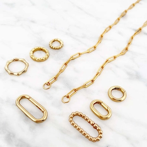 Gold plated link chain necklace with spring ring clasp and textured charms on marble
