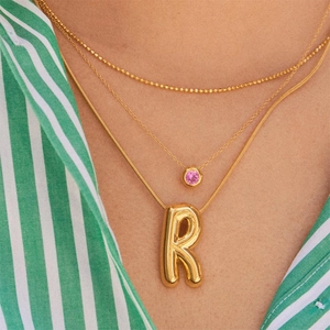Three-layer gold necklace set featuring birthstone pendant and letter R charm on a model