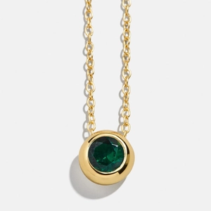 Macro shot of a bezel-set green gemstone pendant on a polished gold chain necklace