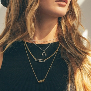 Close-up of layered mixed-metal necklaces with carabiner clasp and heart pendant details