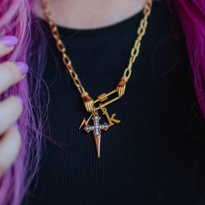 Gold chunky chain necklace with cross pearl and letter K charms on a black knit top