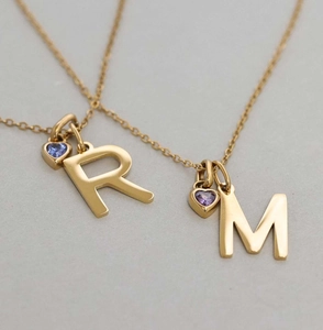 Detail of gold letter R and M pendants with tiny heart-shaped birthstones and fine chain