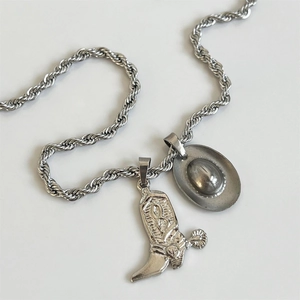 Vue détaillée des pendentifs botte et chapeau de cowboy sur une chaîne en acier