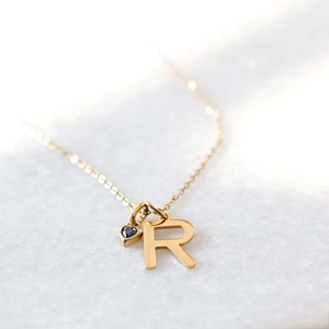 Detail of gold letter R pendant with blue heart gemstone on a fine chain link