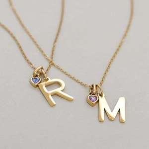 Detail of gold-plated R and M initial necklaces with heart-shaped gemstone pendants
