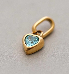 Macro shot of heart-shaped gold-plated pendant with a light blue gemstone inlay