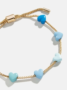 Detalle de una pulsera ajustable de oro con dijes de corazón en degradado azul