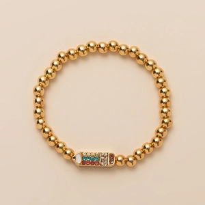 Golden beaded bracelet for girls with rainbow rhinestone rectangle charm on beige surface