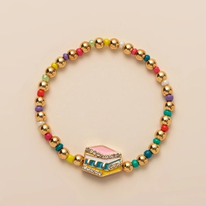 Detail of beaded bracelet with rainbow cake charm, gold beads and colorful enamel