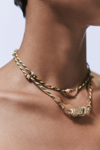Detail einer geflochtenen Halskette mit goldenem Stern- und Mond-Tarot-Zylinderanhänger