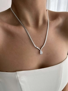 Detail of a silver snake chain necklace with a water drop shaped zircon on a model