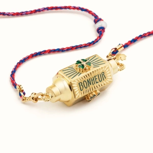 Detailaufnahme des geflochtenen Armbands mit goldenem Zylinder und grünem Kleeblatt