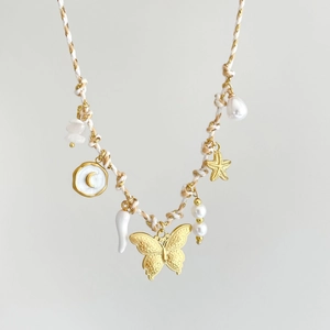 Dettaglio di ciondoli conchiglia stella marina farfalla su collana boho intrecciata
