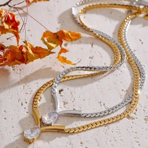 Gold and silver drop zircon pendant necklace with flat snake chain on stone background