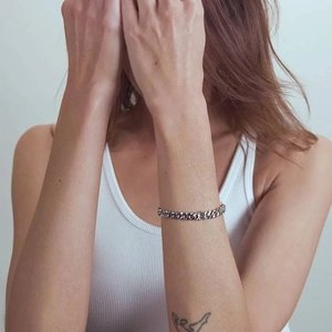 Macro detail of a silver-colored cuban link bracelet on a female model's wrist