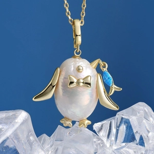 Dettaglio del ciondolo pinguino con perla barocca e pesce blu su una catena in oro 18K