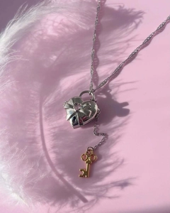 Detalle del collar con relicario de corazón plateado, gema rosa y dije de llave dorada