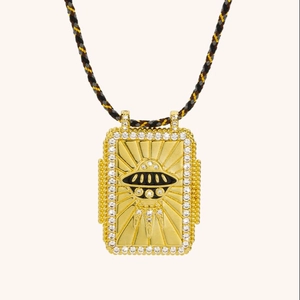 Macro detail of golden rectangular UFO tarot pendant with sparkling zircons and woven cord