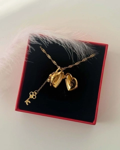 Primer plano del collar con relicario de corazón dorado y llave en estuche de regalo