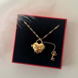 Collar de medallón de corazón dorado con gema rosa y lazo en una caja de regalo roja