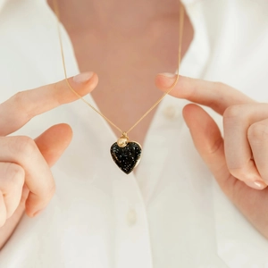 Gros plan du médaillon en forme de cœur sur une chaîne dorée porté sur une chemise blanche